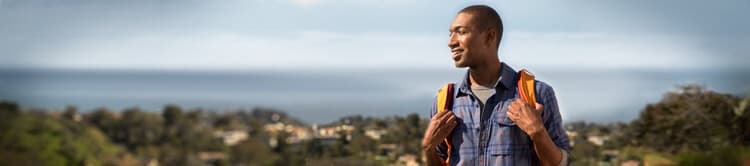 Man smiling while holding his backpack.